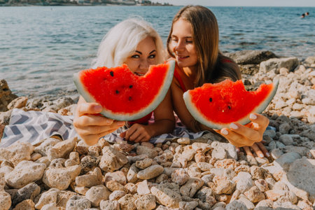 Watermelon Beach Summer: Two women enjoy watermelon slices on a sunny beach during summer vacation.の写真素材