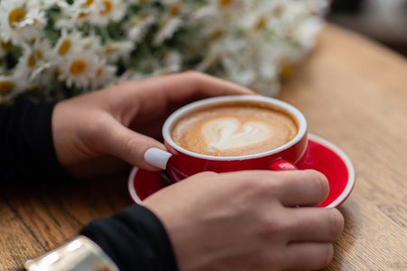 Cappuccino Hands Daisies: Woman holds latte art drink at cafe with flowers for relaxed morningの写真素材