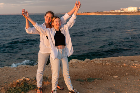 Couple Beach Sunset Romance - Young couple holding hands and celebrating at sunset on a cliff overlooking the ocean.の写真素材