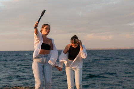 Women Beach Sunset Dance - Two women in white shirts dance on the beach at sunset with a black bat...