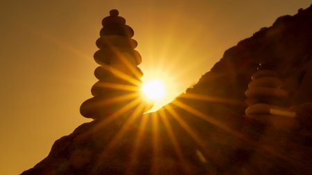 Stones cairn sunset, balanced stacked rocks silhouetted by bright sun rays over a tranquil mountain