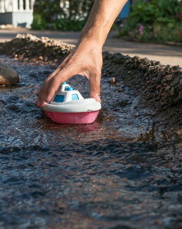Close up of male hand holding plastic toy boat in the river stream. Playing the game.の写真素材