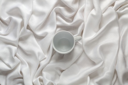 White ceramic empty coffee cup on the silk white fabric. Top viewの写真素材