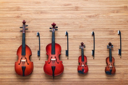 Set of four toy string musical orchestra instruments: violin, cello, contrabass, viola on a wooden background. String Quartet. Music concept. Cello and three violins, all vintage instruments.の写真素材