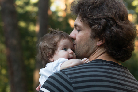 Dad holding his little blue-eyed daughter in his arms for a walk in the park. Summer day, family nature walk, sunnyの写真素材