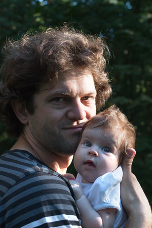 Dad is holding a daughter in his arms for a walk in the park. Spring day, family walk in nature, sunnyの写真素材