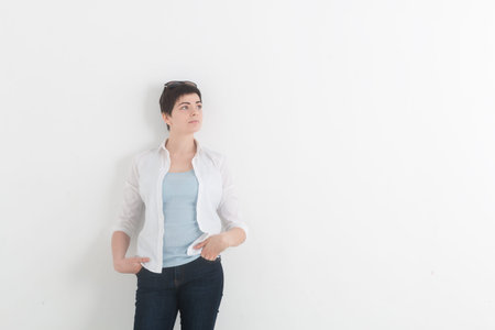 Fashion young woman wearing dark blue jeans and white shirt with sunglasses on her head looking up and dreaming with hands in her pocketsの写真素材