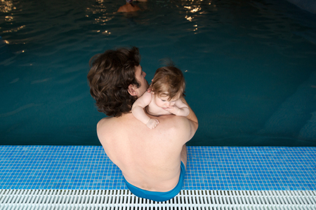 Family of father and his little daughter sitting at edge of swimming pool. Young father and his little cute newborn baby together in spa hotel. Dad holding child adorable girl on arms. Family relaxingの写真素材
