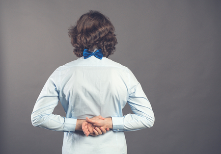 Back view of man in blue shirt and bow tie. Standing young guy. Rear view people collection. Backside view of person. Isolated over grey background. A male stands with his hands folded back in lock.の写真素材