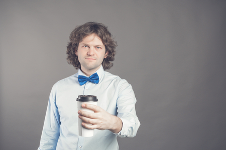 Portrait of happy handsome man in blue shirt and bow tie with paper cup of morning coffee. Good morning with tea. Take away coffee, time for coffee break. Waiter offers coffee to go. Toned Copy spaceの写真素材
