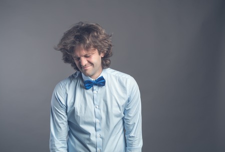 Portrait of unhappy hophead man standing and looking aside with melancholy. Isolated on grey background wearing blue shirt and bow tie. Hunched shoulders lowered Poorly sleeping or insomnia concept.の写真素材