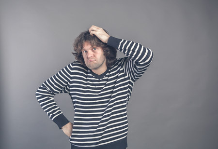 Puzzled guy with messy hair, frowning and looking unsatisfied scratching head, thinking deeply about something on grey wall background. Human facial expression, emotion, feeling, sign body language.の写真素材