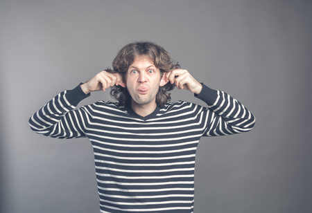 Man making silly monkey face isolated on grey background. Guy grimaces monkey. Funny male holding his ears and shows tongue looks like monkey, pretending chimpanzee, young man entertaining childrenの写真素材
