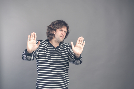 Attractive brunet male shows refusal gesture, curly man does not want to participate in meeting, says: It is not for me, leave me in piece, has angry expression, poses against grey studio backgroundの写真素材