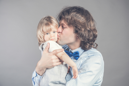 Father with his young baby cuddling and kissing her on cheek. Happy parenthood, love. Bunch of kisses from daddy makes his kid girl bored. Tenderness concept. Child is tired of hugging and embracingの写真素材