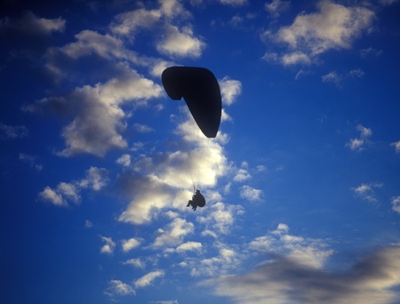 Silhouette of paraglider with two person against the cloudy blue sky.のeditorial素材