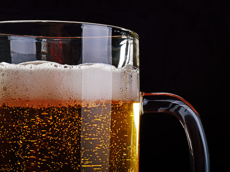 A mug of light beer with froth on black background.の写真素材
