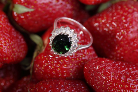 Beautiful gold ring with green gemstone and small diamonds on a red strawberry.の写真素材
