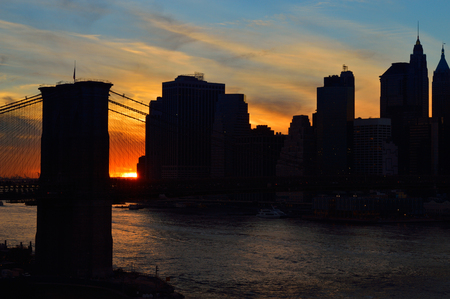 Silhouette of Manhattan skyline with Brooklyn Bridge at sunset.の写真素材