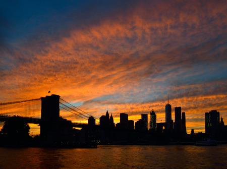 Silhouette of Manhattan skyline with Brooklyn Bridge at sunset.の写真素材