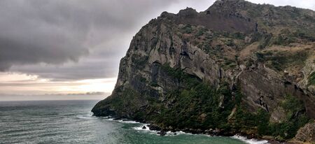 Cliff with green grass on the sea shore on a rainy cloudy dayの写真素材