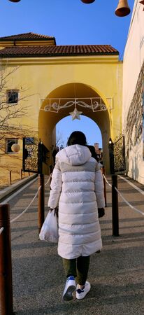 A woman in big white winter jacket with back to the camera entering a yellow decorated gateの写真素材