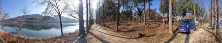 Gorgeous panoramic winter scenery with the sun beautifully illuminating the lake and the sand road surrounded by trees in Nami Island, South Koreaの写真素材