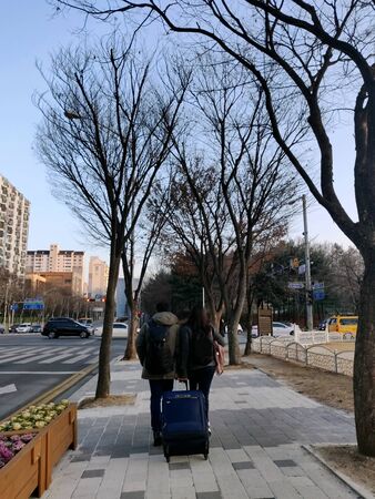 An Indian couple walking in the stret of Seoul in winters hand-in-hand along with their travel bags and luggage in South Koreaの写真素材