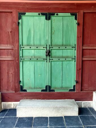 A wooden green door with red wall with an old ancient lock and blue floor in the frontの写真素材