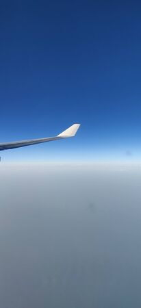 Airplane wing seen from the window of the airplane amidst blue sky and above cloudsの写真素材