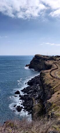 Rock bech and wavy dirt country path of songaksan mountain looking at the brightest blue ocean in Jeju Island, South Koreaの写真素材