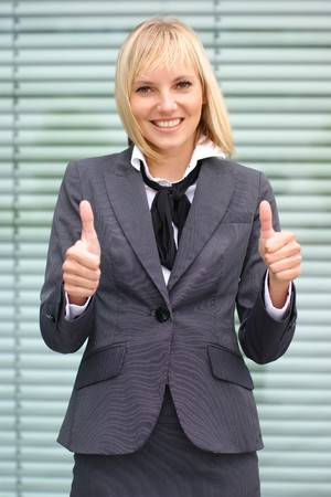 A young and happy blond businesswoman is holding thumbs up as a sign on successの写真素材