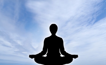 Human silhouette meditating over sky backgroundの写真素材