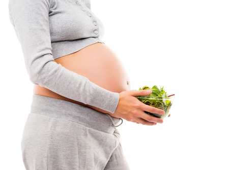 A young and pregnant woman in sporty clothes holding a fresh green salad. Image isolated on a white background.の写真素材