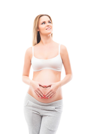 A young and beautiful pregnant woman making the heart sign with her arms isolated on whiteの写真素材