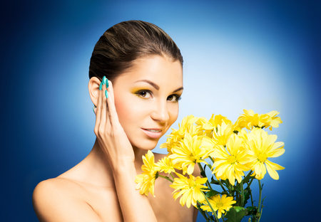 Young and beautiful girl with the bouquet of chrysanthemum over blue backgroundの写真素材