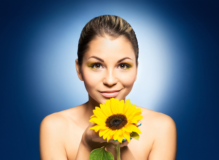 Young and beautiful girl with the sunflower over blue backgroundの写真素材