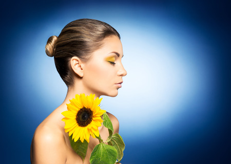 Young and beautiful girl with the sunflower over blue backgroundの写真素材