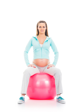 Young and healthy pregnant woman training with a fitness ball isolated on whiteの写真素材