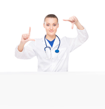 Young, professional and cheerful female doctor standing over big blank billboard isolated on whiteの写真素材