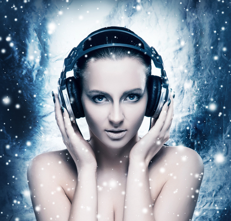 Glamour and bizarre portrait of young and beautiful woman listening to the music over creative winter backgroundの写真素材