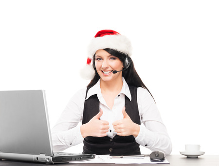 Young, confident and beautiful support operator in Christmas hat working in a call centerの写真素材