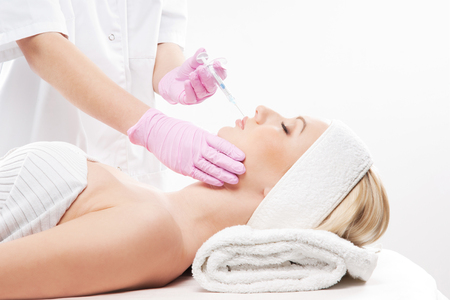 Beautiful woman gets an injection in her face isolated on whiteの写真素材
