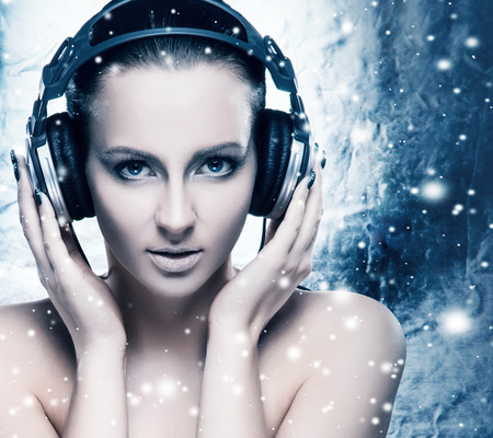 Glamour and bizarre portrait of young and beautiful woman listening to the music over creative winter backgroundの写真素材