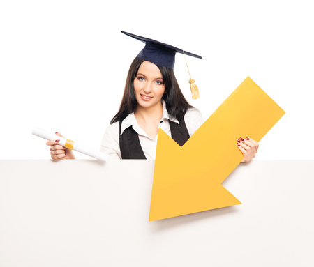 Young, beautiful and happy graduate girl pointing on a blank banner and smiling isolated on whiteの写真素材