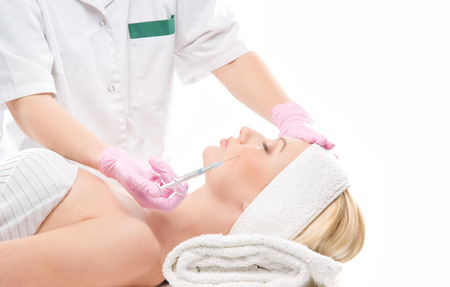 Beautiful woman gets botox injection in her face isolated on whiteの写真素材