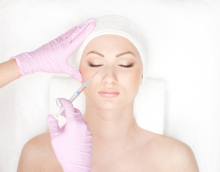 Beautiful woman gets an injection in her face isolated on whiteの写真素材