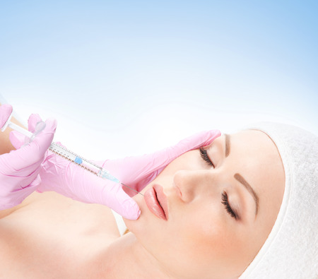 Beautiful woman gets an injection in her face isolated on whiteの写真素材