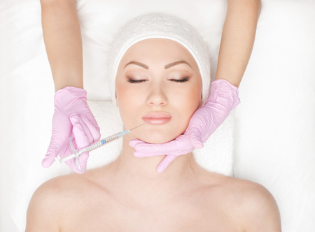 Beautiful woman gets an injection in her face isolated on whiteの写真素材