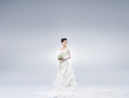 Young and beautiful bride standing with the flower bouquet over the grey background. There is a blank space for any text.の写真素材